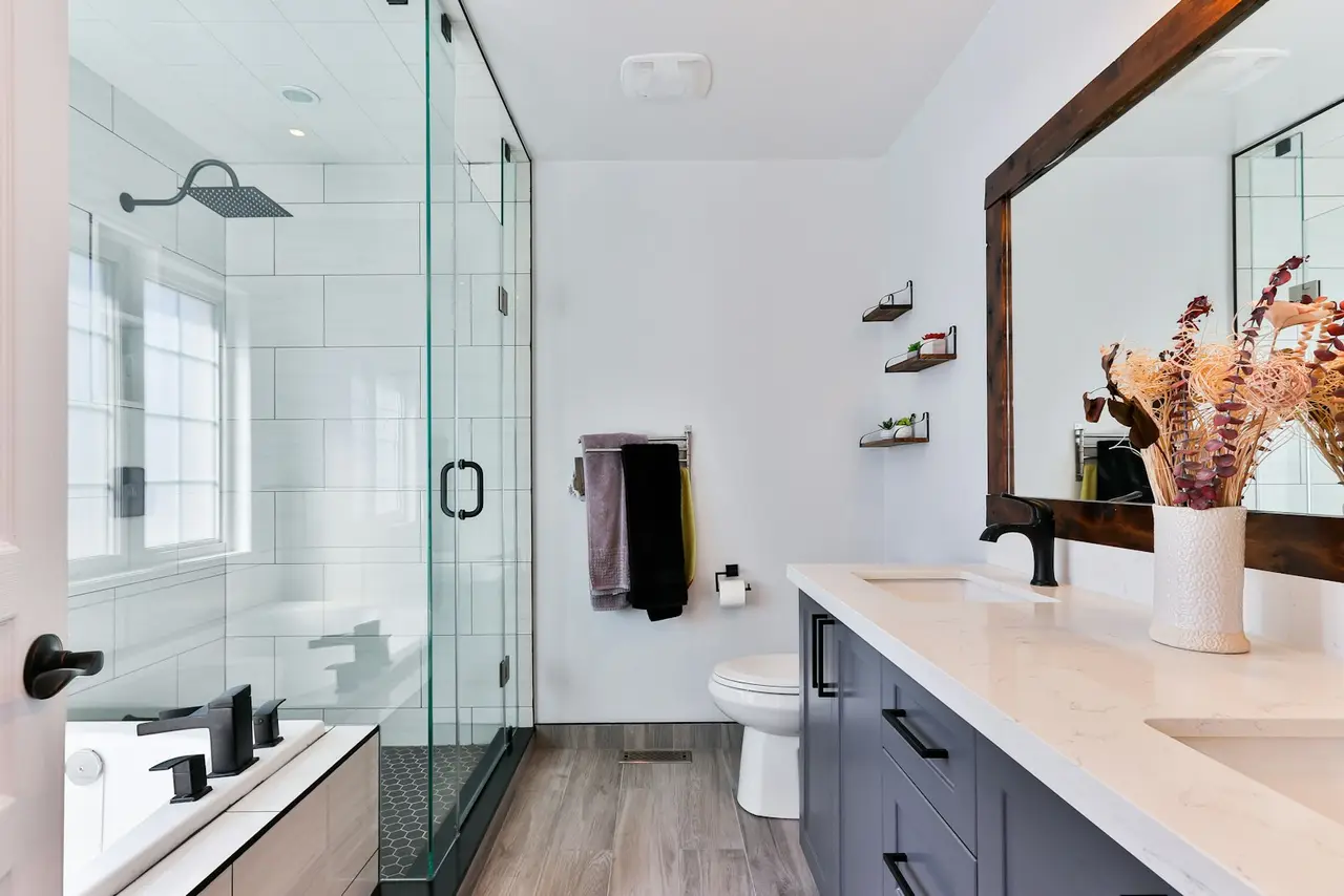 A compact modern bathroom with a glass shower, floating shelves and a vanity with drawers